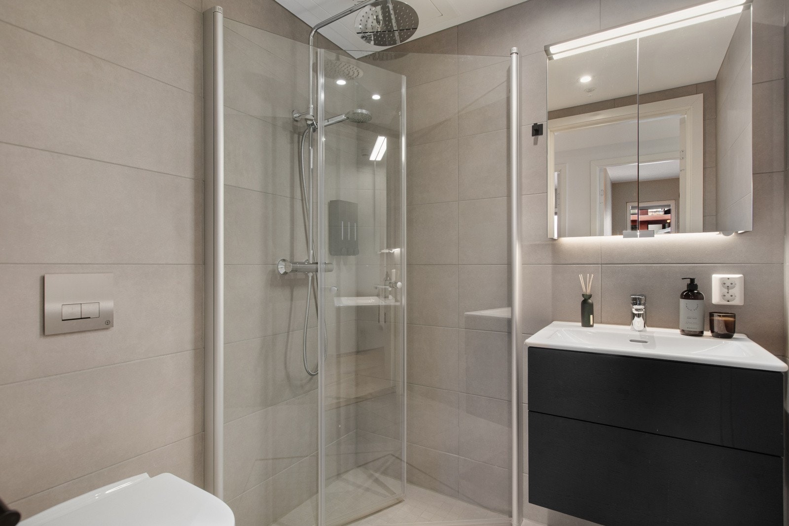 Det mindre baderommet har servant, veggmontert toalett og dusj med praktiske hjørneløsninger, og kombinerer funksjonalitet med moderne design. Galleribilde