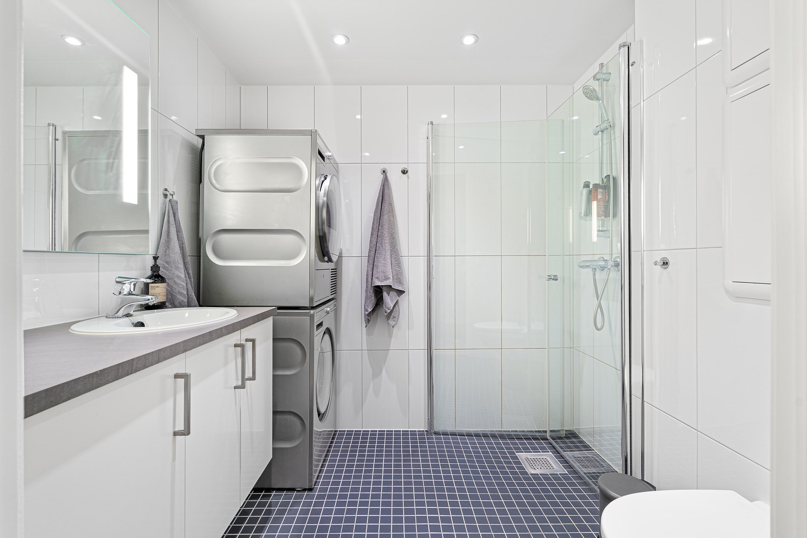 Videre er badet innredet med servantskap med speil og lys, vegghengt toalett og dusjhjørne. Galleribilde