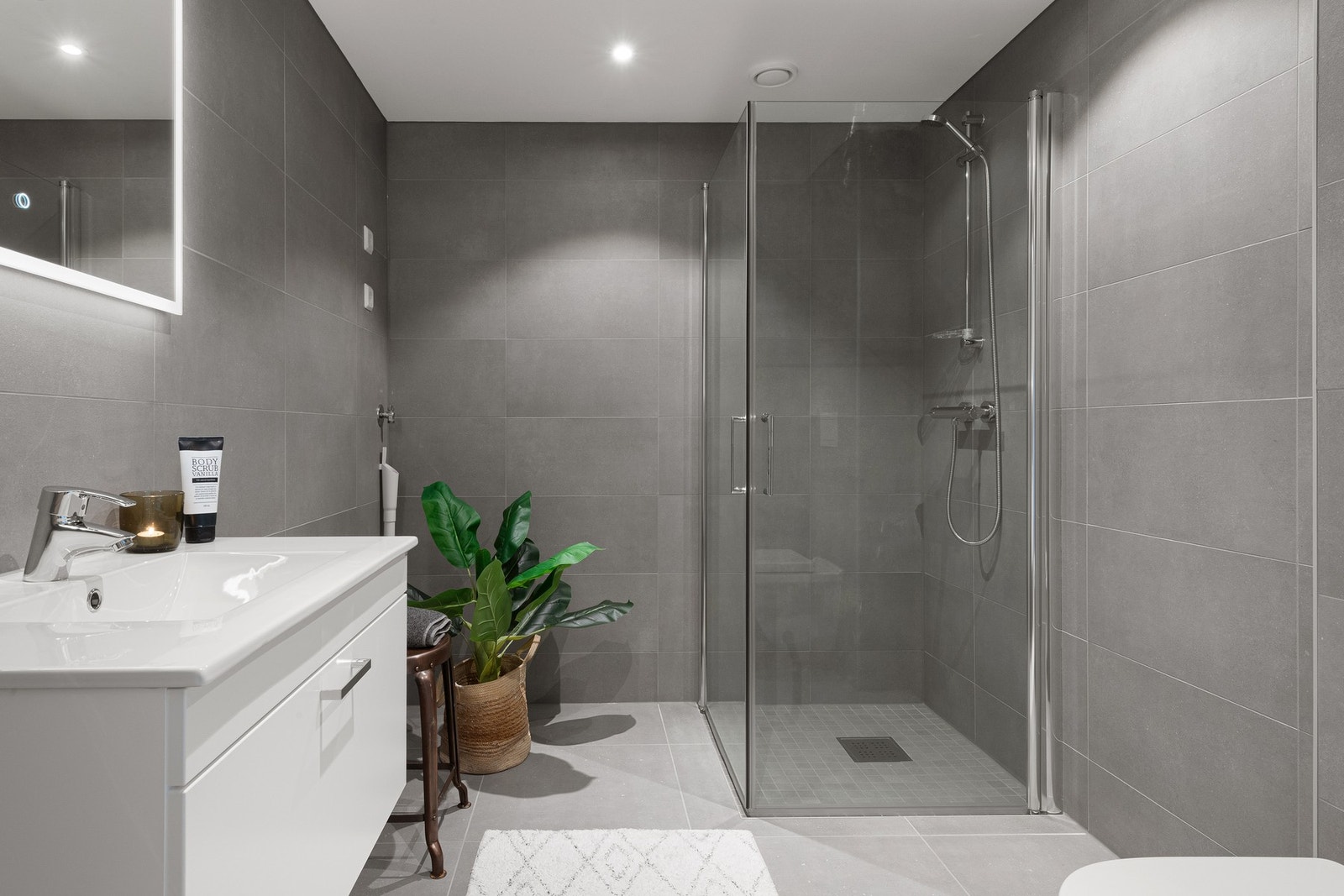 Moderne bad med grå fliser, dusjkabinett med glassvegger og hvit baderomsinnredning. Galleribilde