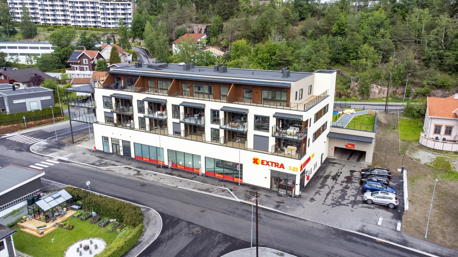 Moderne leilighetsbygg med butikker i første etasje, parkeringsplasser og omgitt av natur. Galleribilde