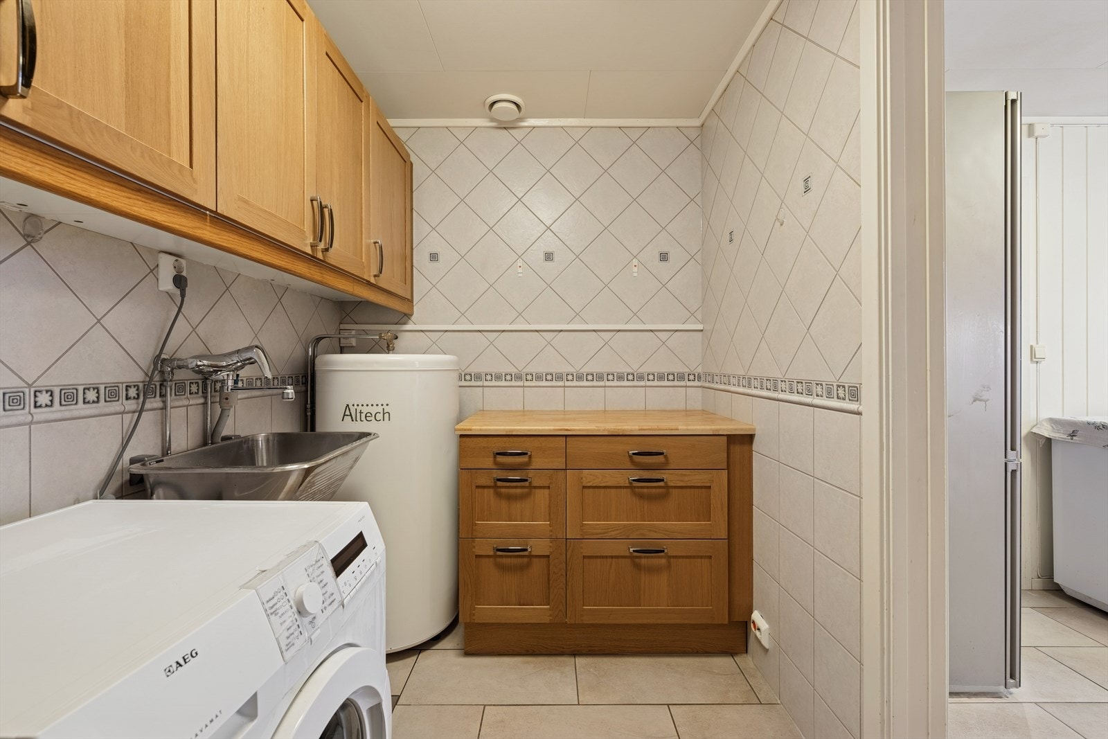 Vaskerommet har flislagte vegger og gulv, og er utstyrt med overskap, benk med skuffer og utslagsvask. Det er også opplegg for vaskemaskin. Galleribilde