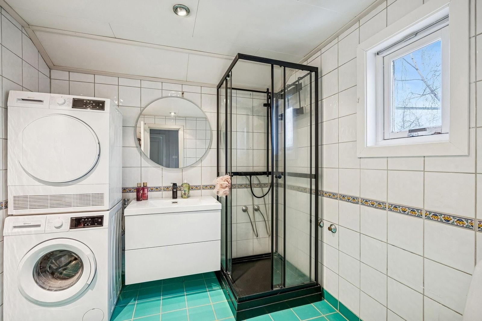 Badet er flislagt og funksjonelt innredet. Rommet er utstyrt med dusjkabinett, servant i baderomsinnredning med skuffer, veggspeil og toalett. Galleribilde