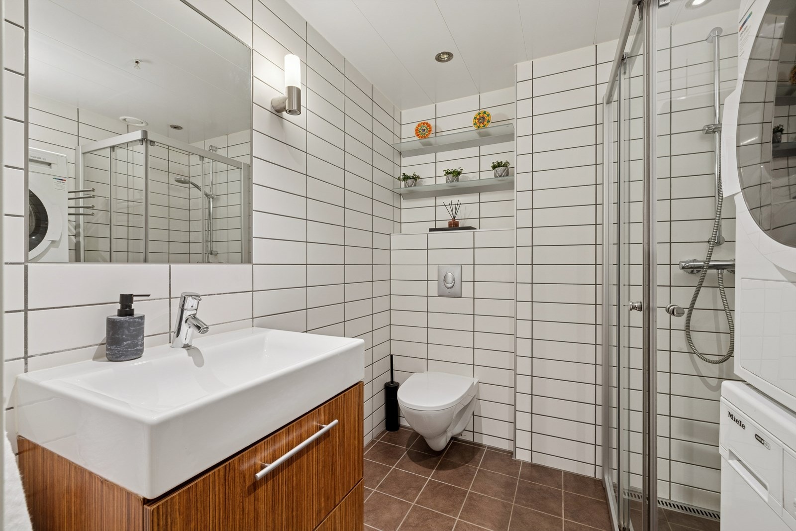 Bad/vaskerommet er flislagt og innredet med vegghengt toalett, servant med servantskap, dusj og opplegg for vaskemaskin. Galleribilde