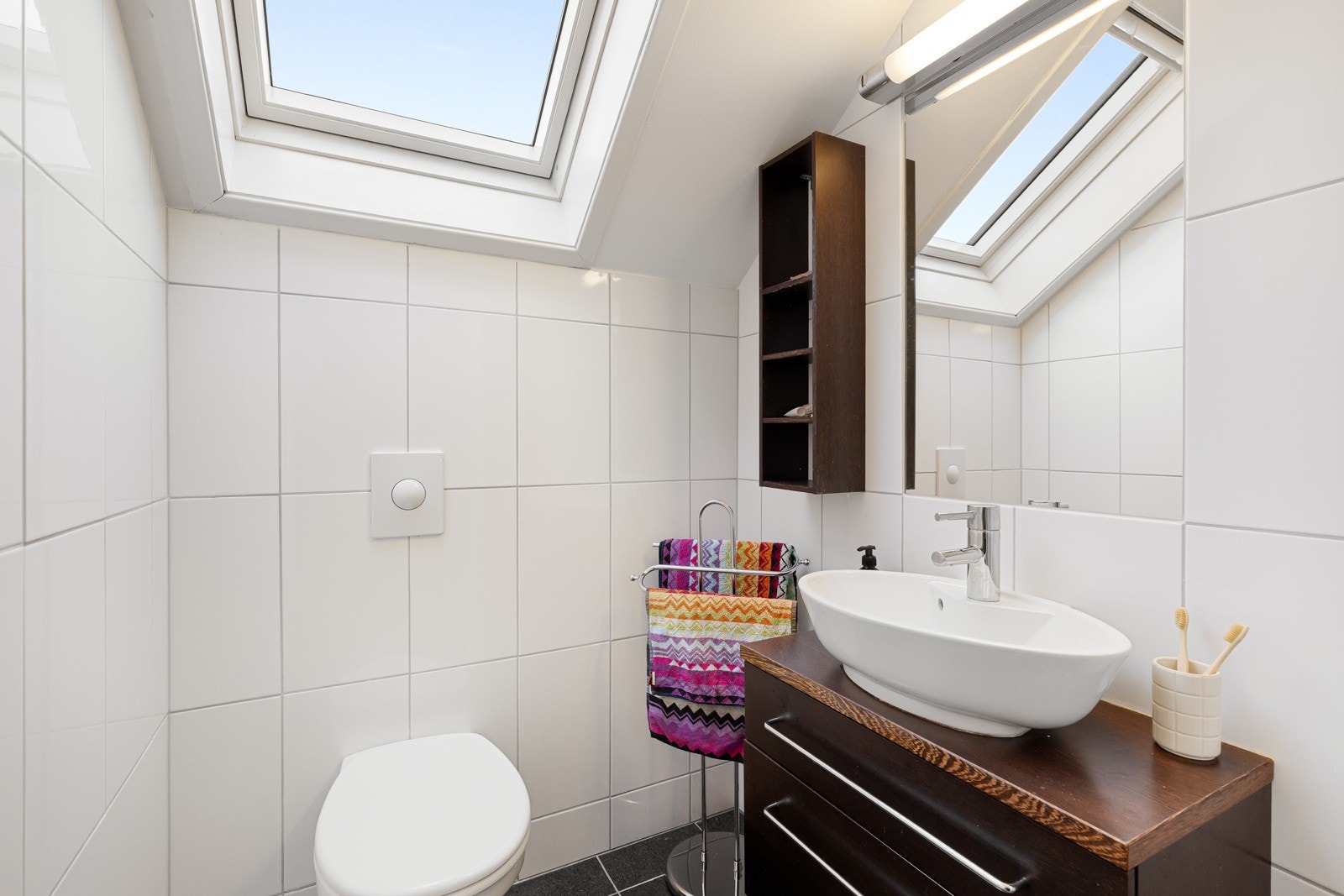 Badet er helfliset og innredet med servant i møbel, speil med belysning, toalett og dusjløsning, og holder en klassisk og tidløs utførelse. Galleribilde