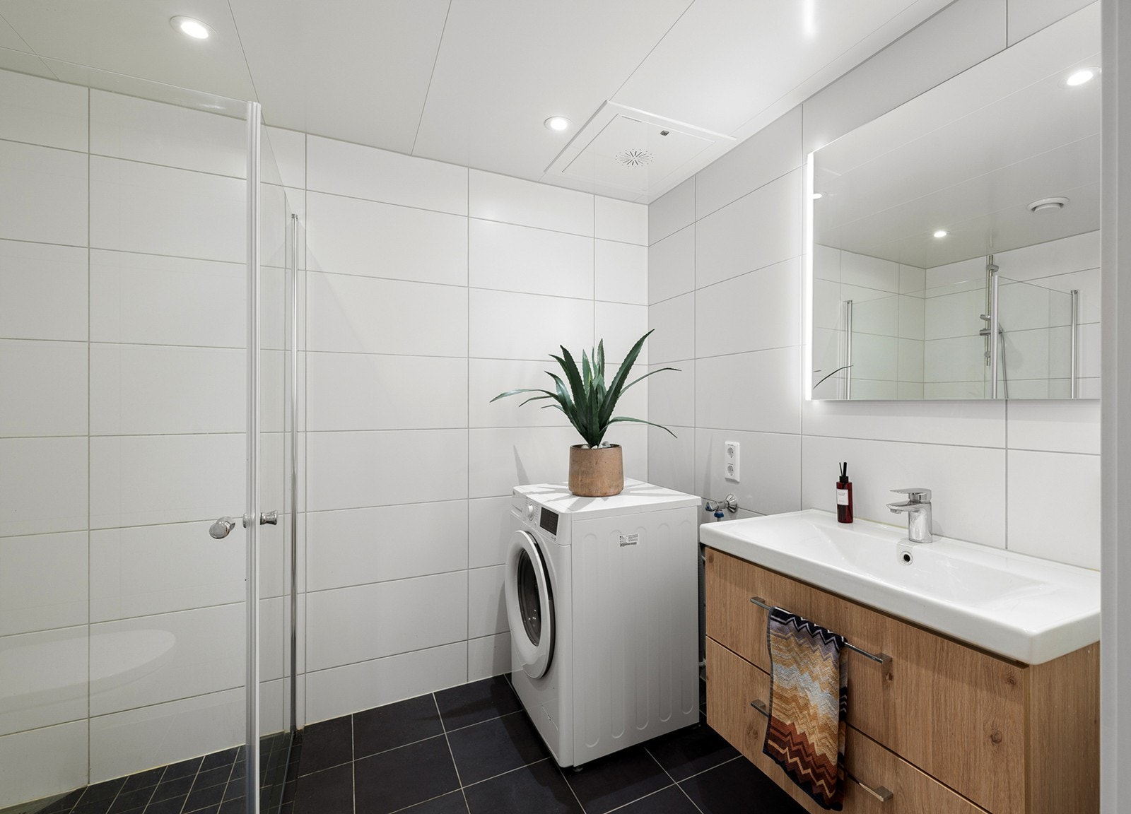 Lyst og moderne bad med store, lyse fliser på vegger og mørke fliser på gulv. Gulvvarme og downlights gir en lun og behagelig atmosfære. Galleribilde