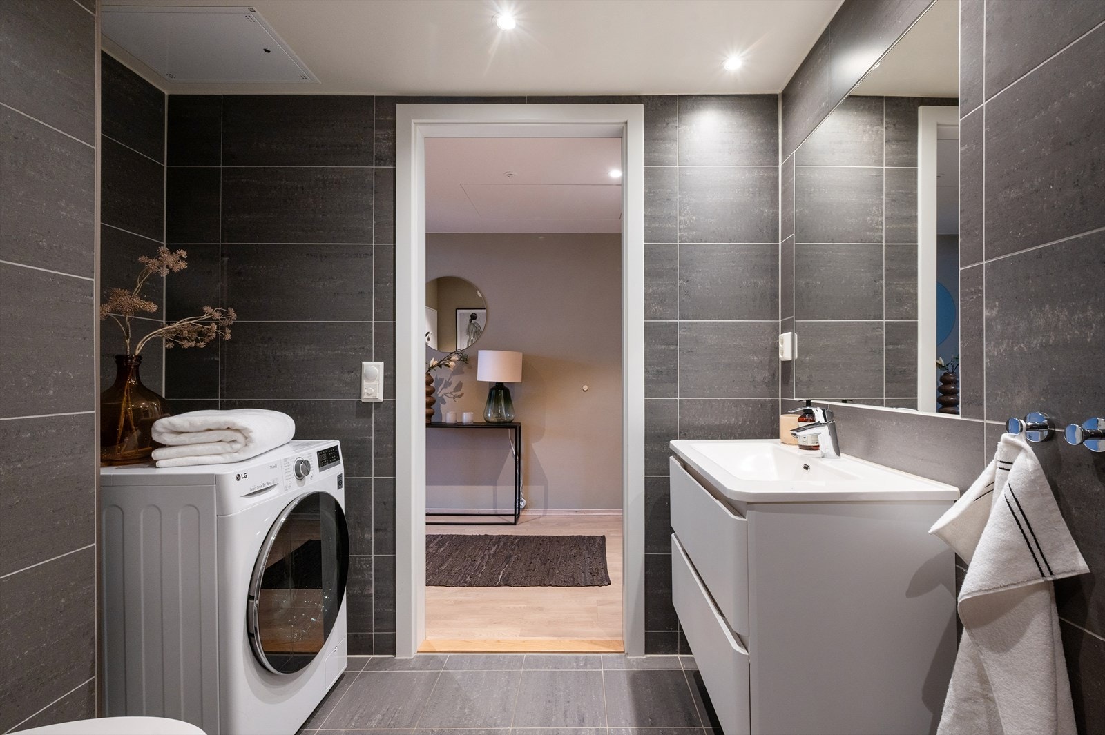 Badet har opplegg for vaskemaskin, ventilasjon, flislagt gulv med gulvvarme, flislagte vegger og malte plater med integrerte downlights i himlingen. Galleribilde