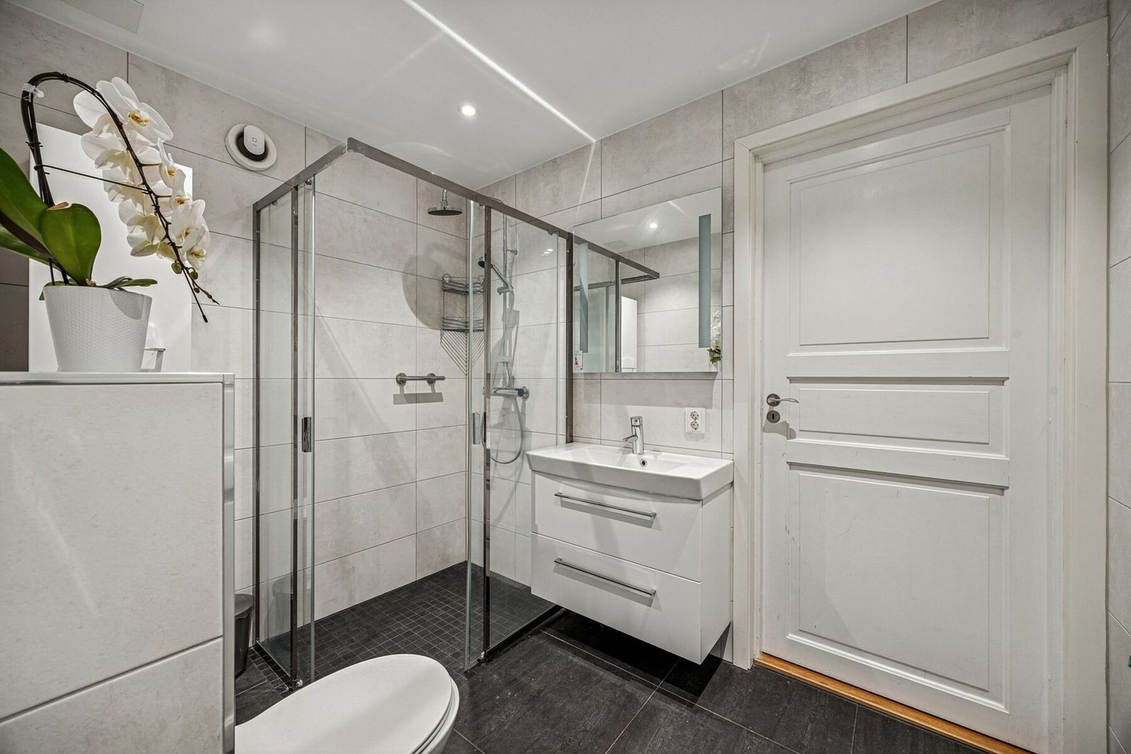 Flislagt bad som er innredet med dusjhjørne, servant i innredning og vegghengt toalett. Galleribilde