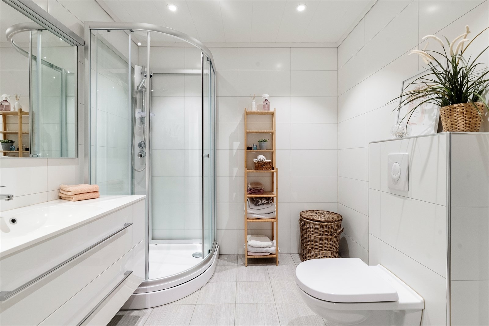 Romslig, helfliset bad med downlights i tak. Vegghengt toalett, dusjkabinett og servantinnredning med skuffer og speil. Galleribilde