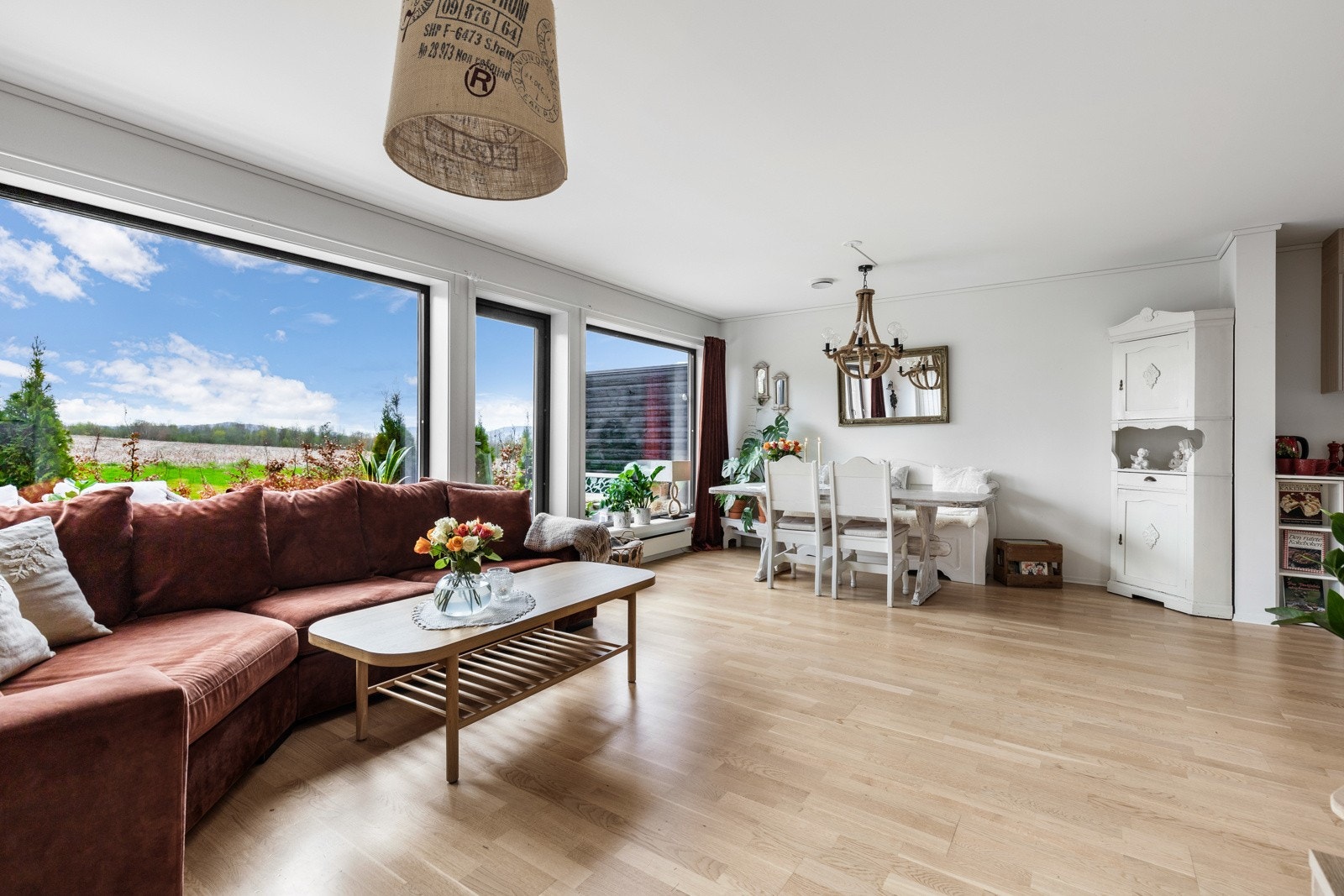 Lys stue med store vinduer, parkettgulv og spiseplass. Utsikt mot grønt landskap. Galleribilde