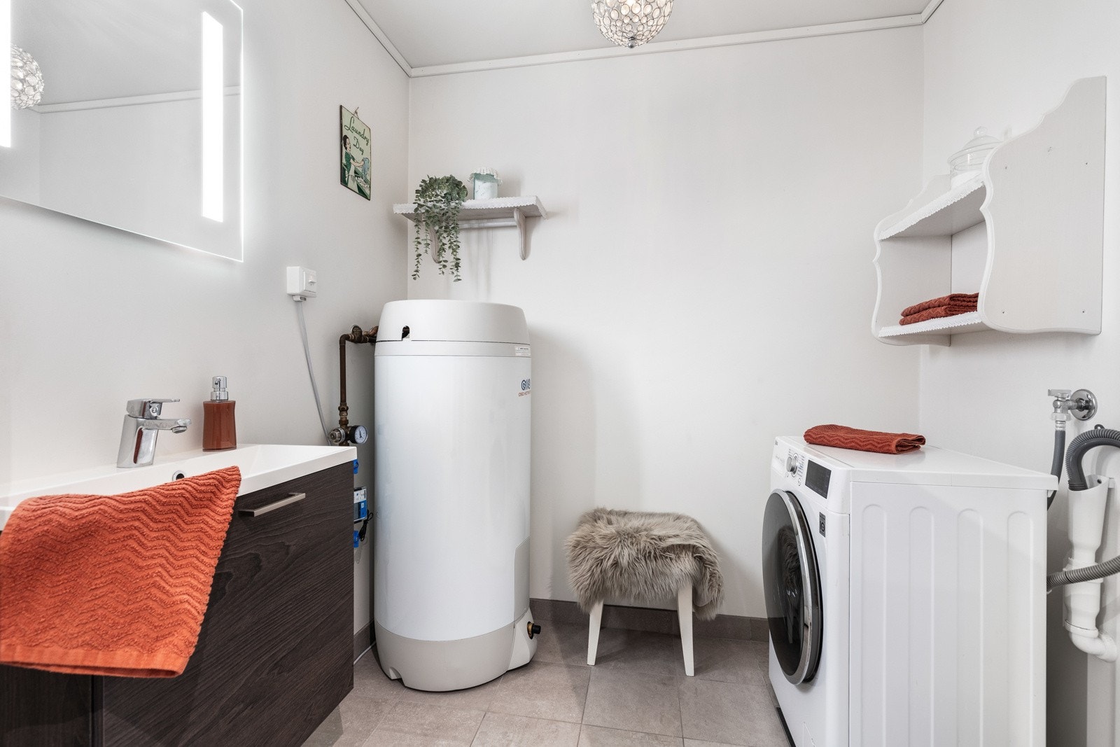 Lyst vaskerom med varmtvannsbereder, vaskemaskin og servant med underskap. Galleribilde