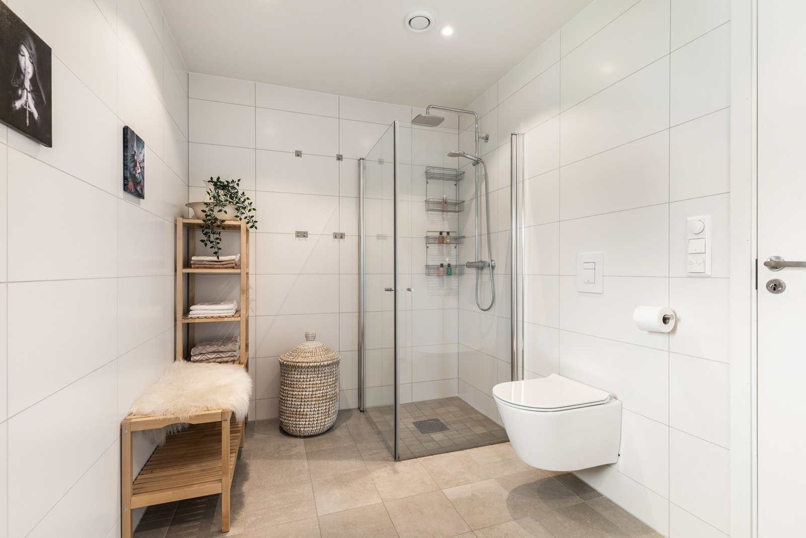 Moderne bad med dusjhjørne og vegghengt toalett, flislagte vegger og gulv, samt plass til praktisk oppbevaringshylle. Galleribilde