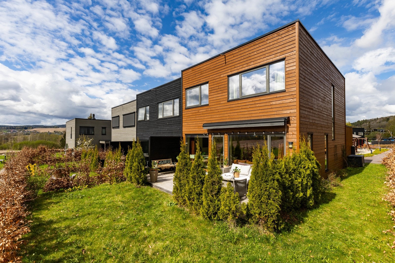 Stokkeveien 8N er et moderne rekkehus, med store vinduer og en liten hage foran. Asfaltert gangvei og blomstrende trær. Galleribilde