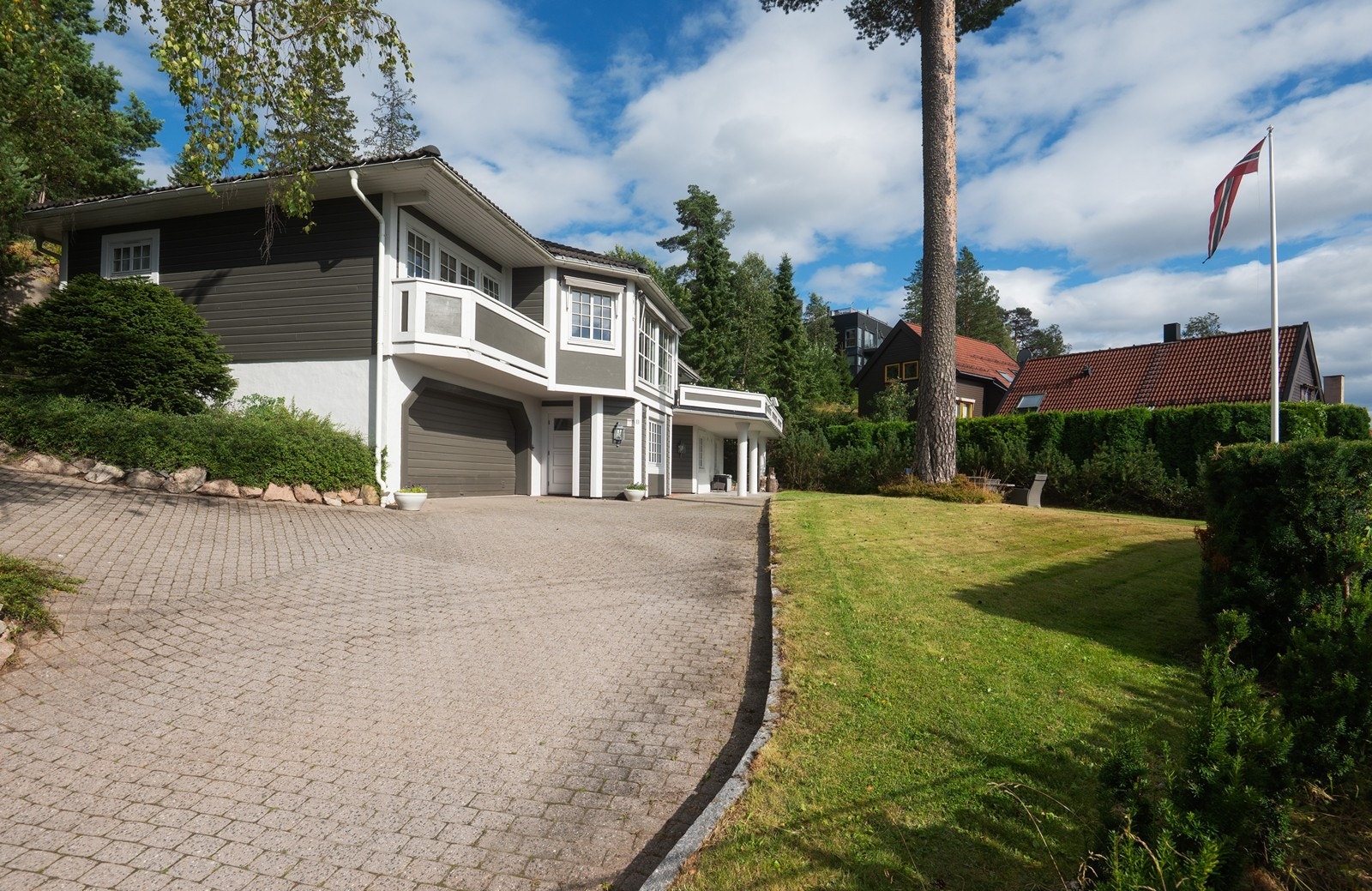 Eiendommen ligger godt tilbaketrukket og høyt hevet over veien skjermet med både gjerde og vintergrønn hekk Galleribilde