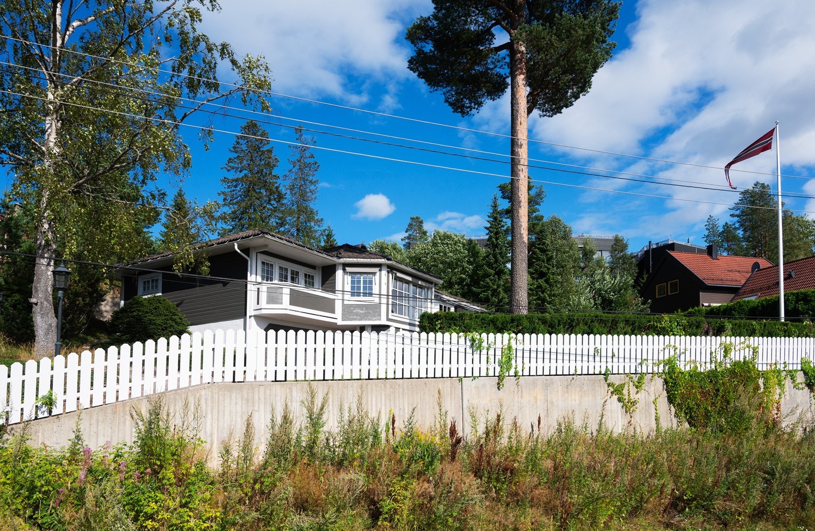 Eiendommen ligger godt tilbaketrukket og høyt hevet over veien skjermet med både gjerde og vintergrønn hekk Galleribilde
