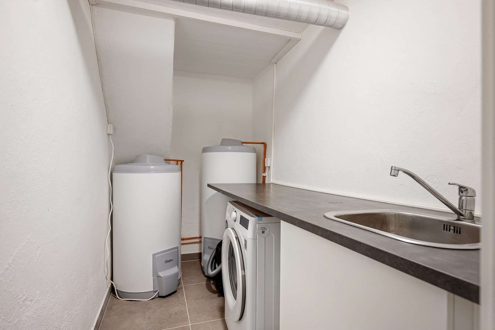 I boligens vaskerom er det opplegg til vaskemaskin og tilgang til boligen og utleiedelens varmtvannstank. Galleribilde