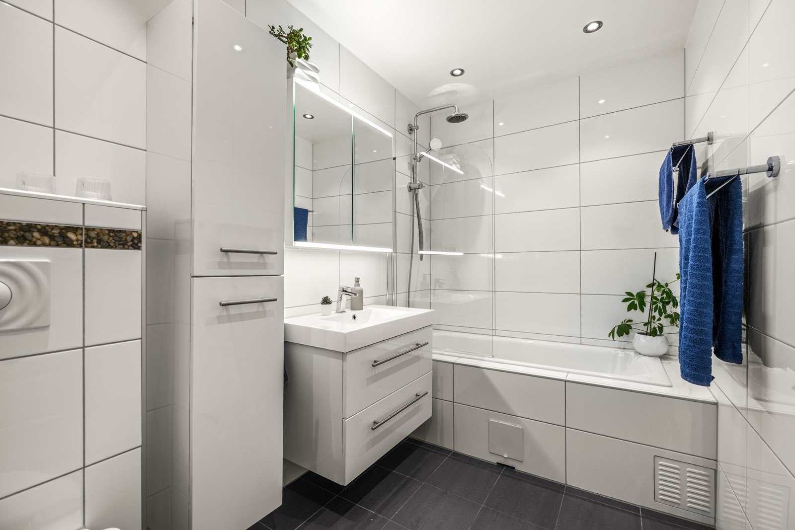 Badet (pusset opp i 2016) har mørke gulvfliser med underliggende varme, hvite veggfliser og malt tak med spottbelysning. Galleribilde