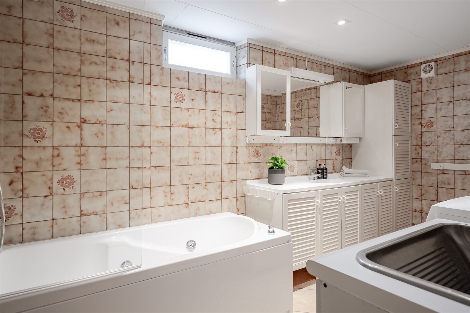 Eldre bad/vaskerom i kjeller med fliser på gulv og vegger, gulvvarme, downlights i himlingen og mekanisk avtrekksvifte. Galleribilde