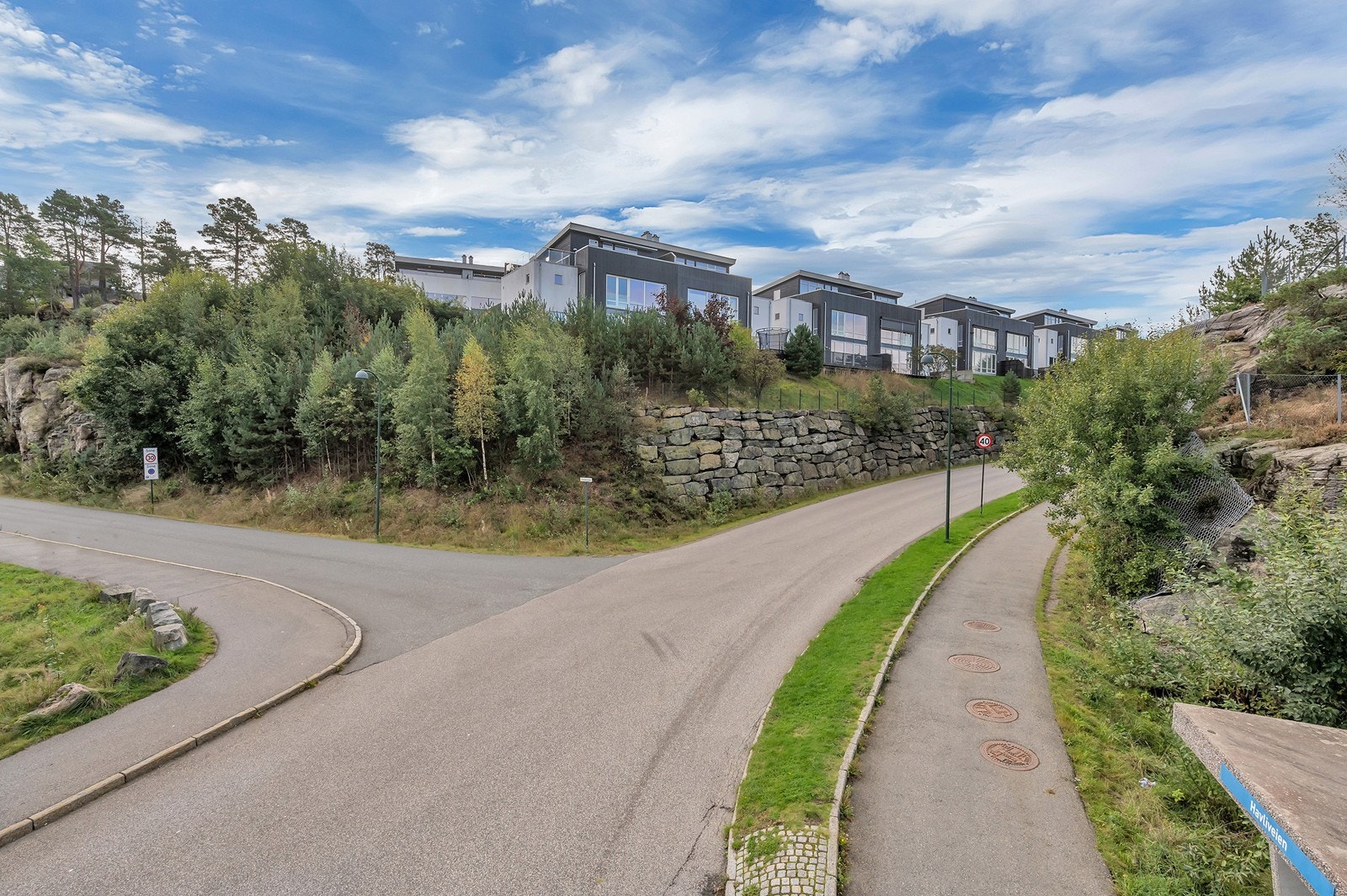 Boligen ligger usjenert til på en opphøyet tomt. Langs veien under i bildet er det rikelig med bussavganger. Galleribilde