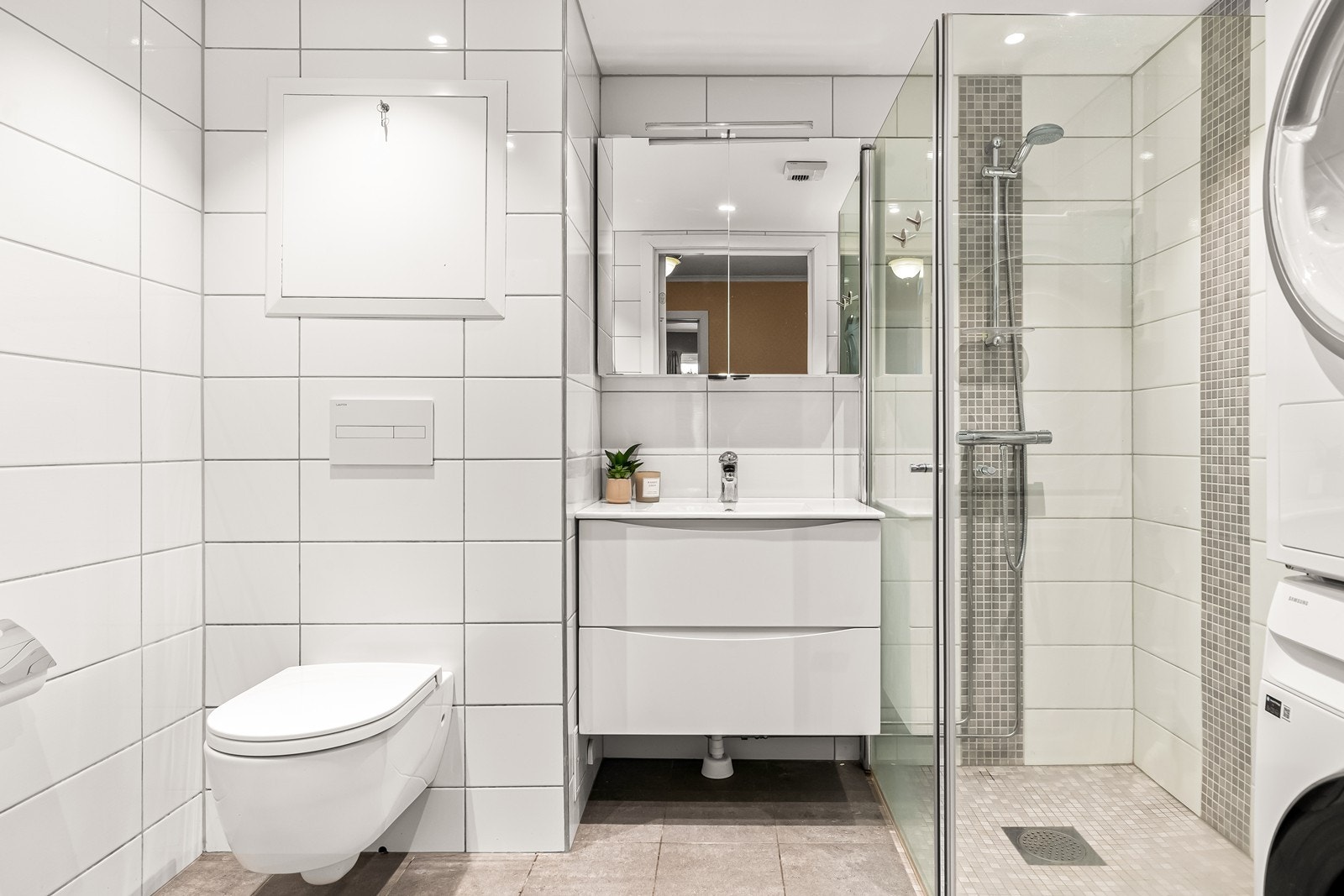 Badet er tidløst innredet med hvite fliser, vegghengt toalett og servantmøbel. Galleribilde