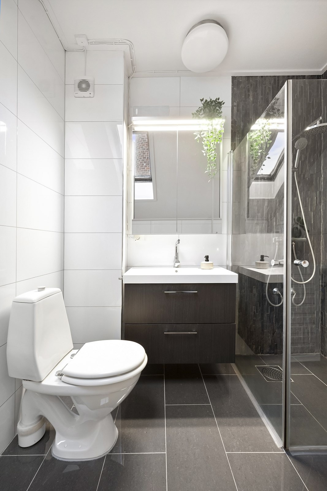 Badet er innredet med gulvstående toalett, dusjhjørne med svingbare glassdører og baderomsinnredning med skuffer, nedfelt servant og speilskap med belysning. Galleribilde