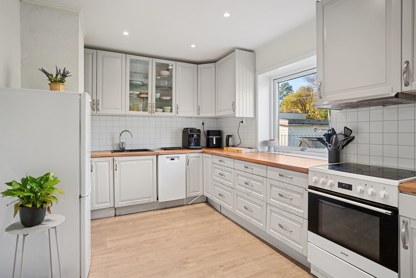 Innholdrsikt kjøkken som har en eldre innredning med profilerte fronter, et overskap som har glassfronter og benkeplaten er av laminat med nedfelt kum i komposittmateriale. Galleribilde