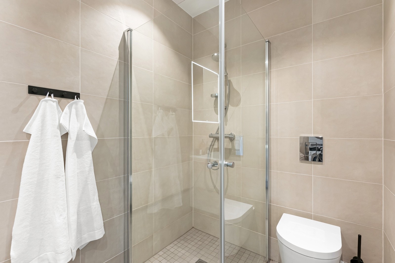 Dusjnisje med innfellbare glassdører og håndholdt dusj - Veggmontert klosett, gulvvarme og downlights. Galleribilde