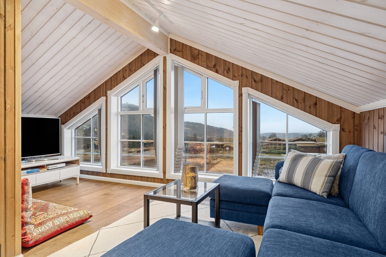 Loftsetasjen utgjør en egen, innbydende sone i hytta, hvor stuen danner et lyst og luftig oppholdsrom med utsikt mot omgivelsene. Galleribilde