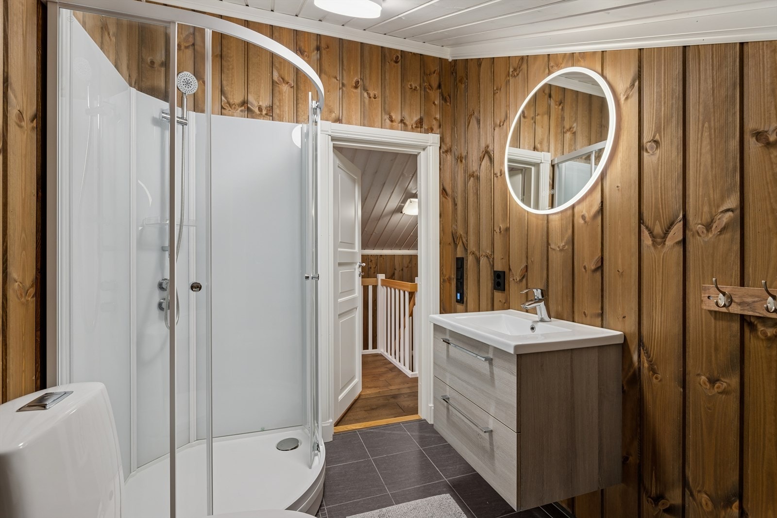 Badet i loftsetasjen er innredet med dusjkabinett, frittstående toalett og servant med underskap og speil med lys. Galleribilde