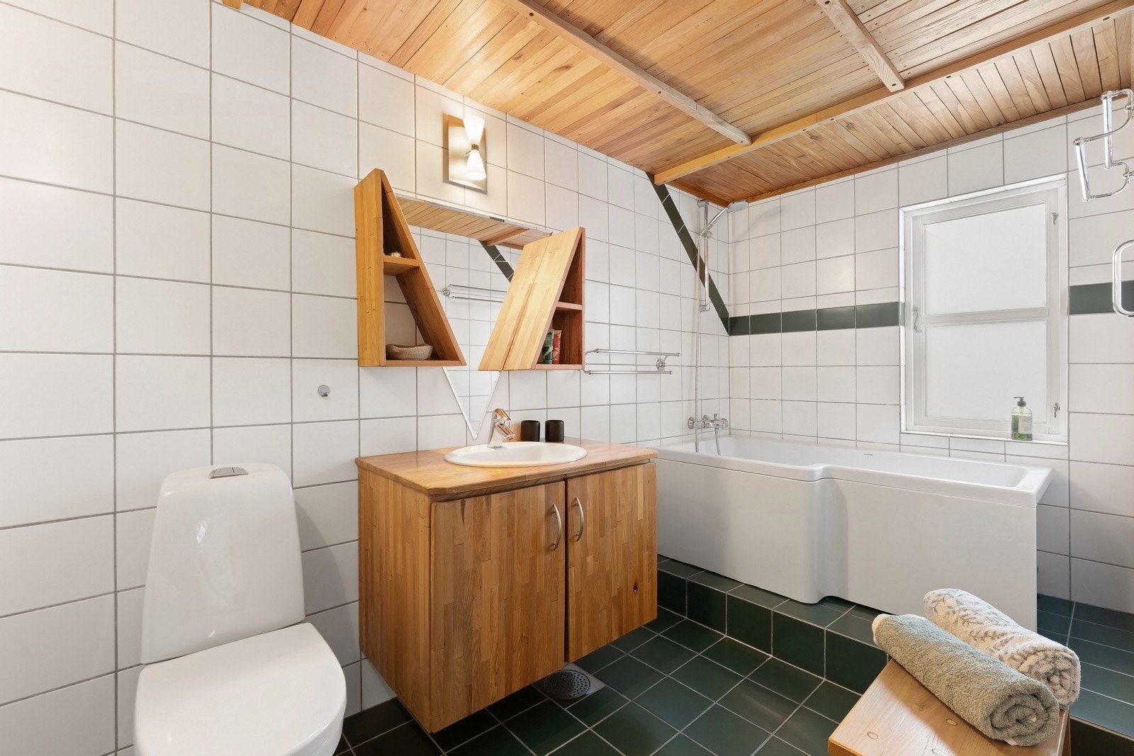 Badet er flislagt med badekar, servant og gulvstående toalett. Galleribilde