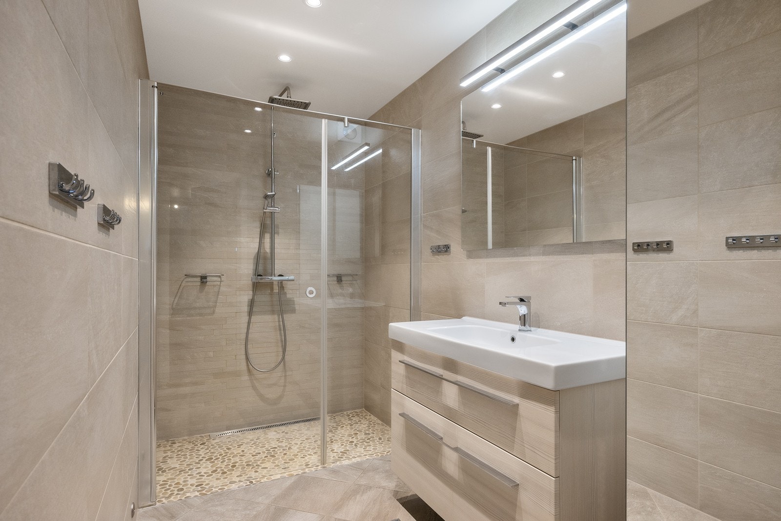 På badet er det downlights og varmekabler, og et stort dusjhjørne har rullestein, slukrenne, regnfallsdusj og svingbar glassdør. Galleribilde