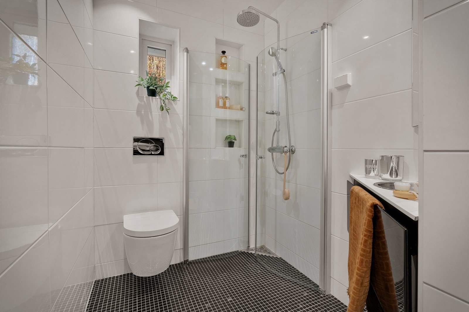 Badet er innredet med veggmontert klosett, servant med underskap og speilskap og dusj med svingbar glassdør. Galleribilde