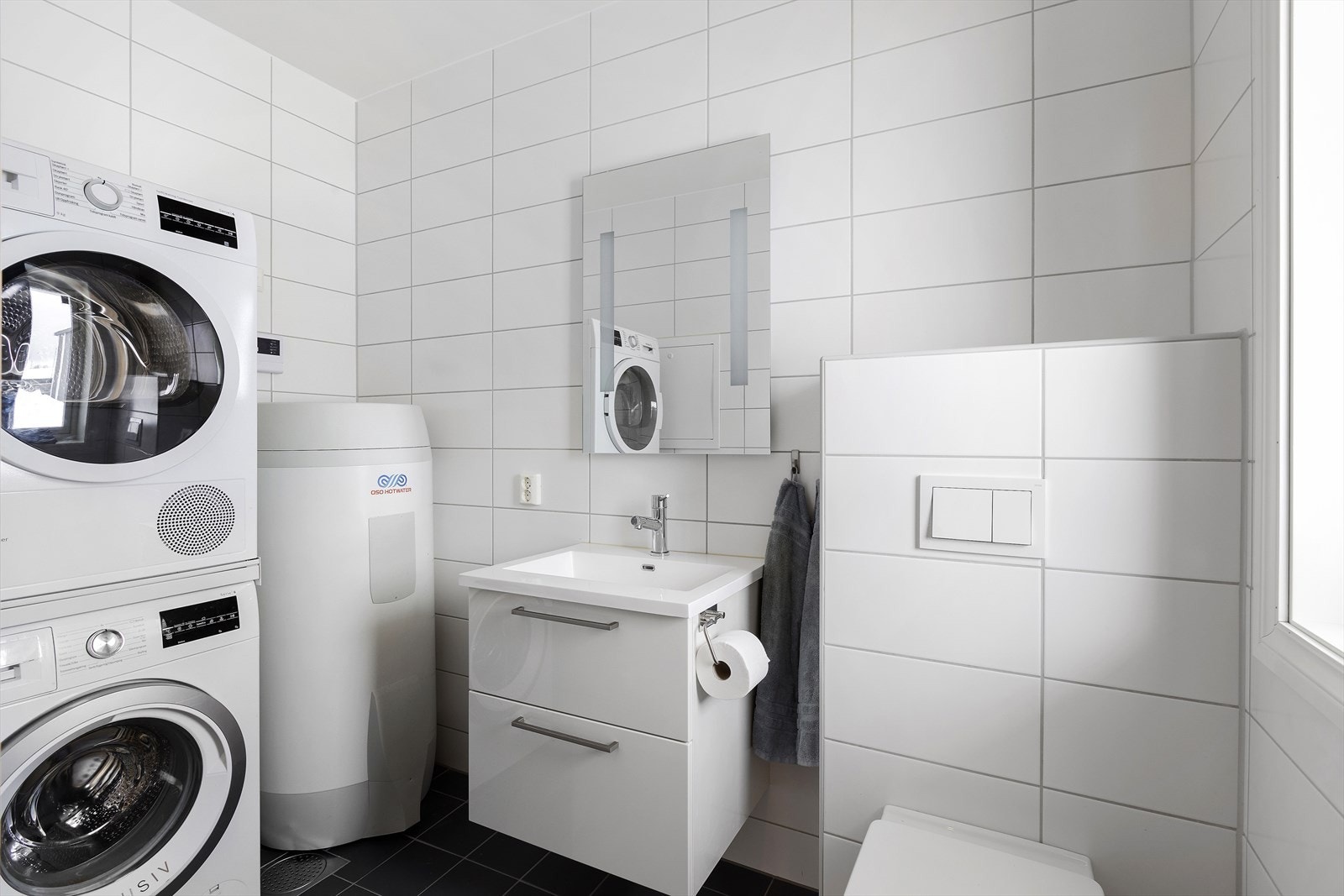 Helfliset med varme i gulv. Vegghengt toalett, servant med skuffeseksjon, speil med belysning, varmtvannstank og opplegg for vaskemaskin/tørketrommel. Galleribilde