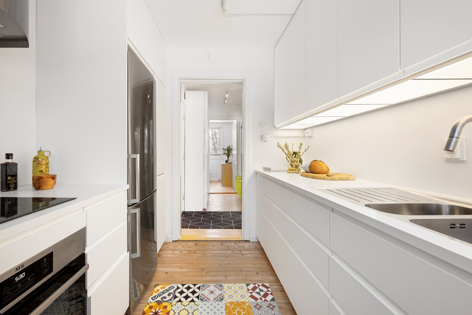 Kjøkkenet er utstyrt med benkebelysning, kullfilterventilator over kokesonen, opplegg for oppvaskmaskin og nisje til kjøleskap. Innredningen har hvite glatte fronter og benkeplate med nedfelt kum i rustfri stål. Galleribilde