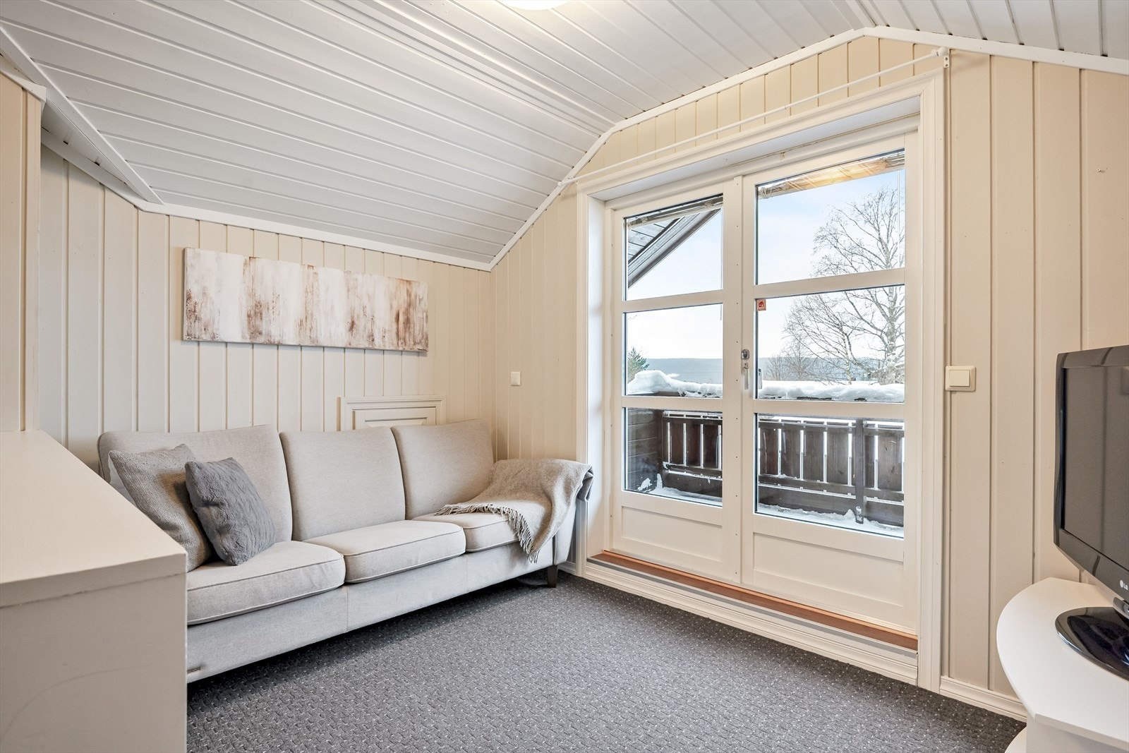 Lys og hyggelig stue med lunt teppegulv og panel på veggene malt i en fin lys farge. Galleribilde