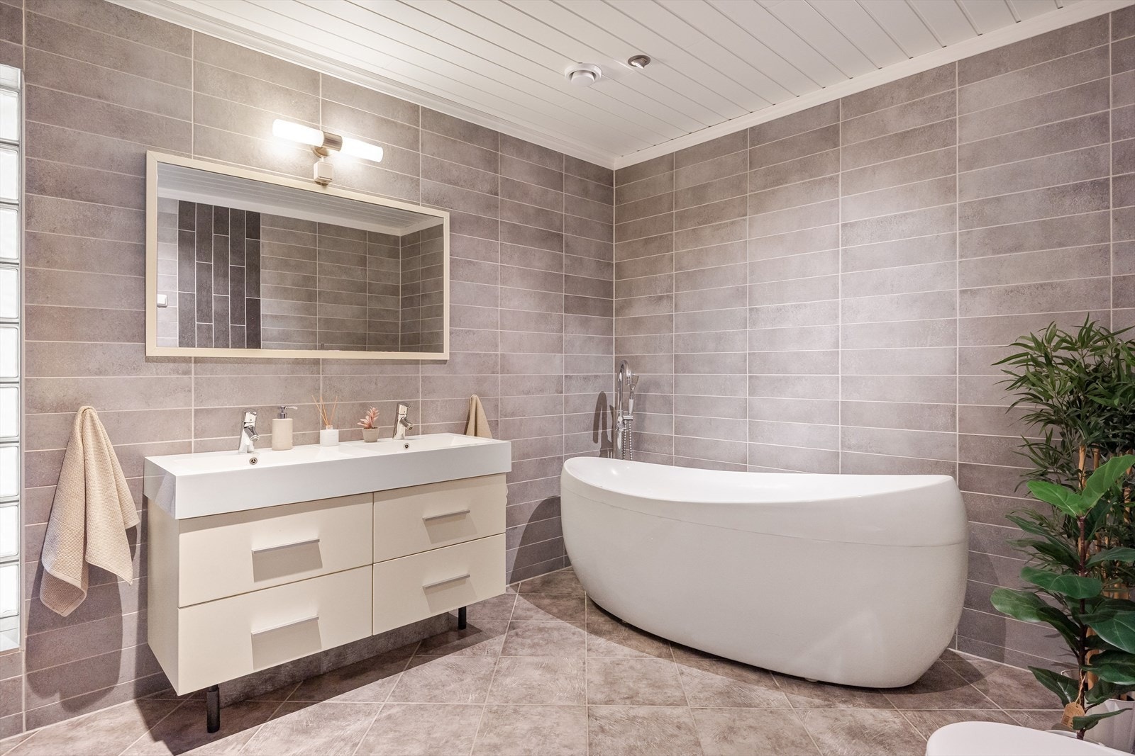 Flott baderomsinnredning med skuffer og ovenpåliggende dobbelservant, speil med belysning over. Galleribilde