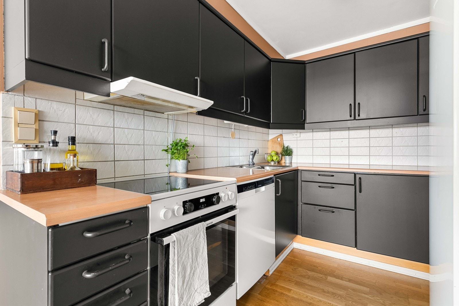 Det er frittstående hvitevarer og lyse fliser mellom overskap og benkeplate. Galleribilde