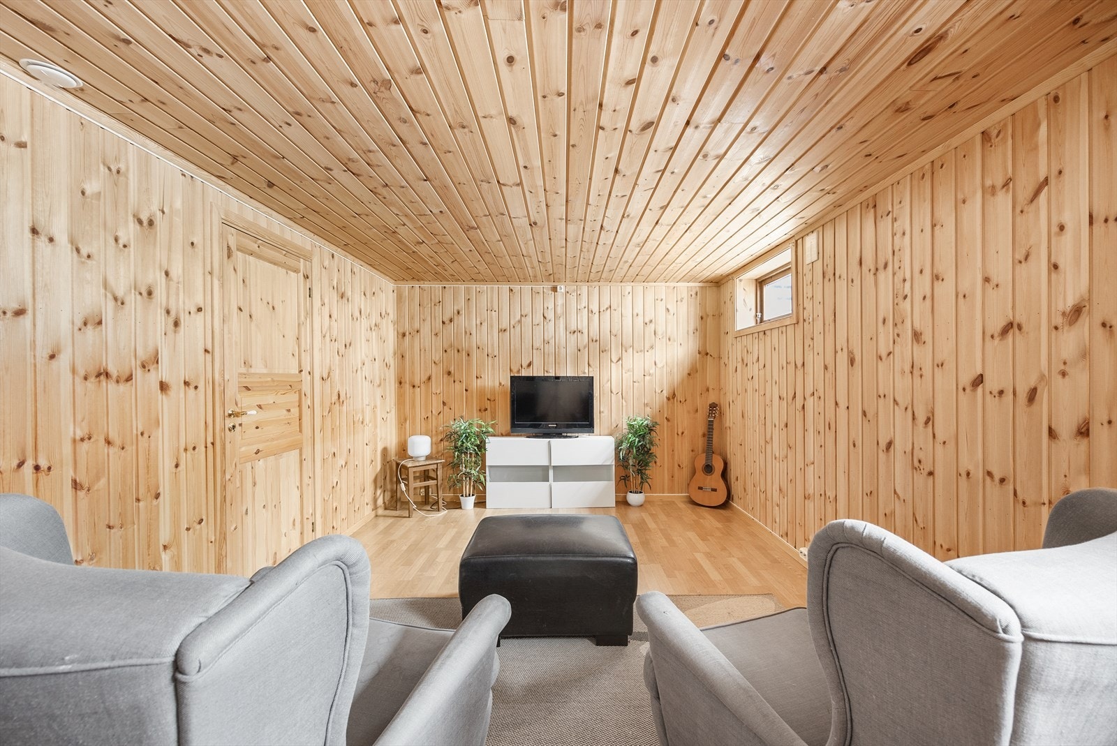 Disponibelt rom innredet som TV-stue med panel på veggene og laminat på gulvet. Galleribilde