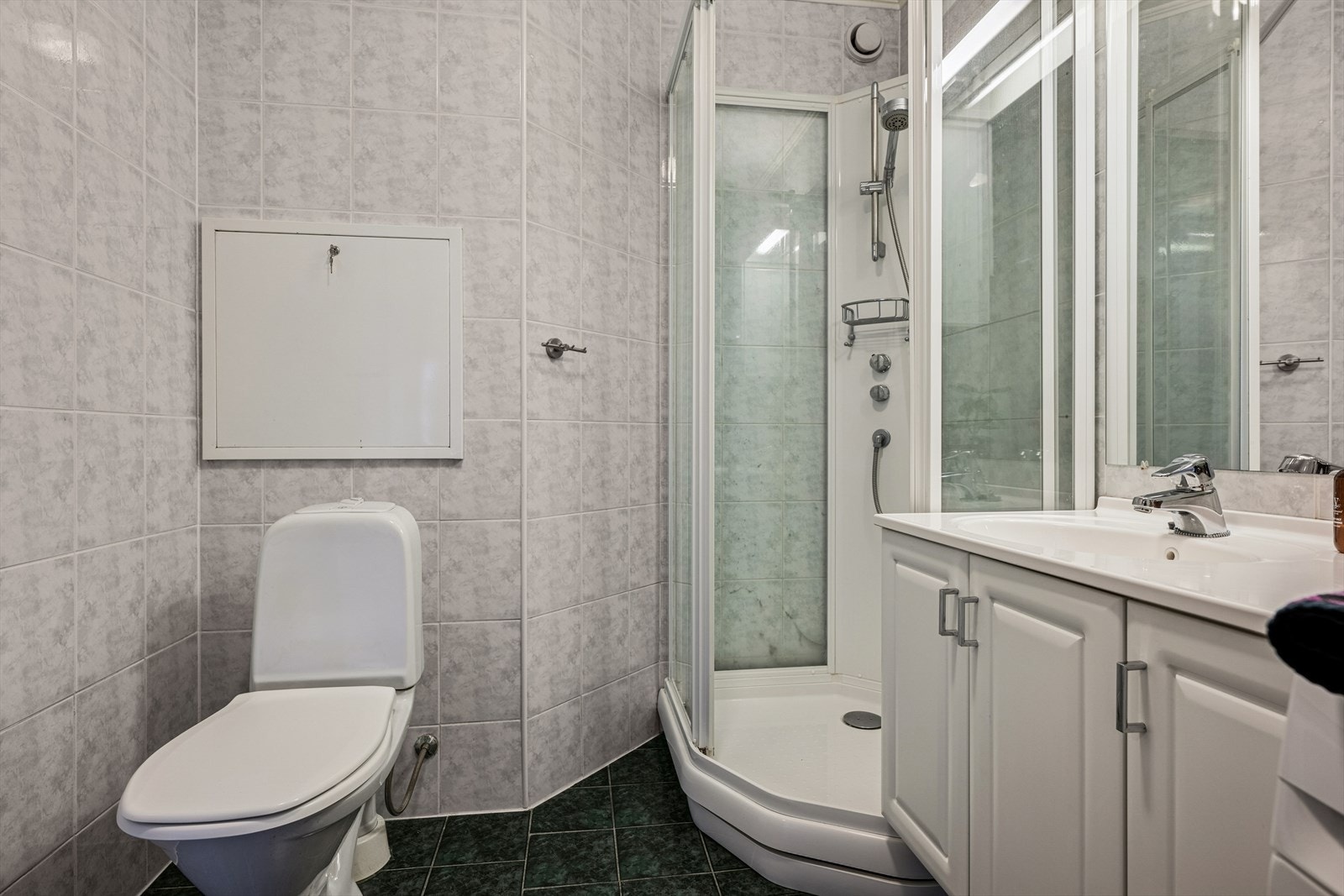 Badet er innredet med servant integrert i baderomsmøbel, toalett og dusjkabinett. Galleribilde