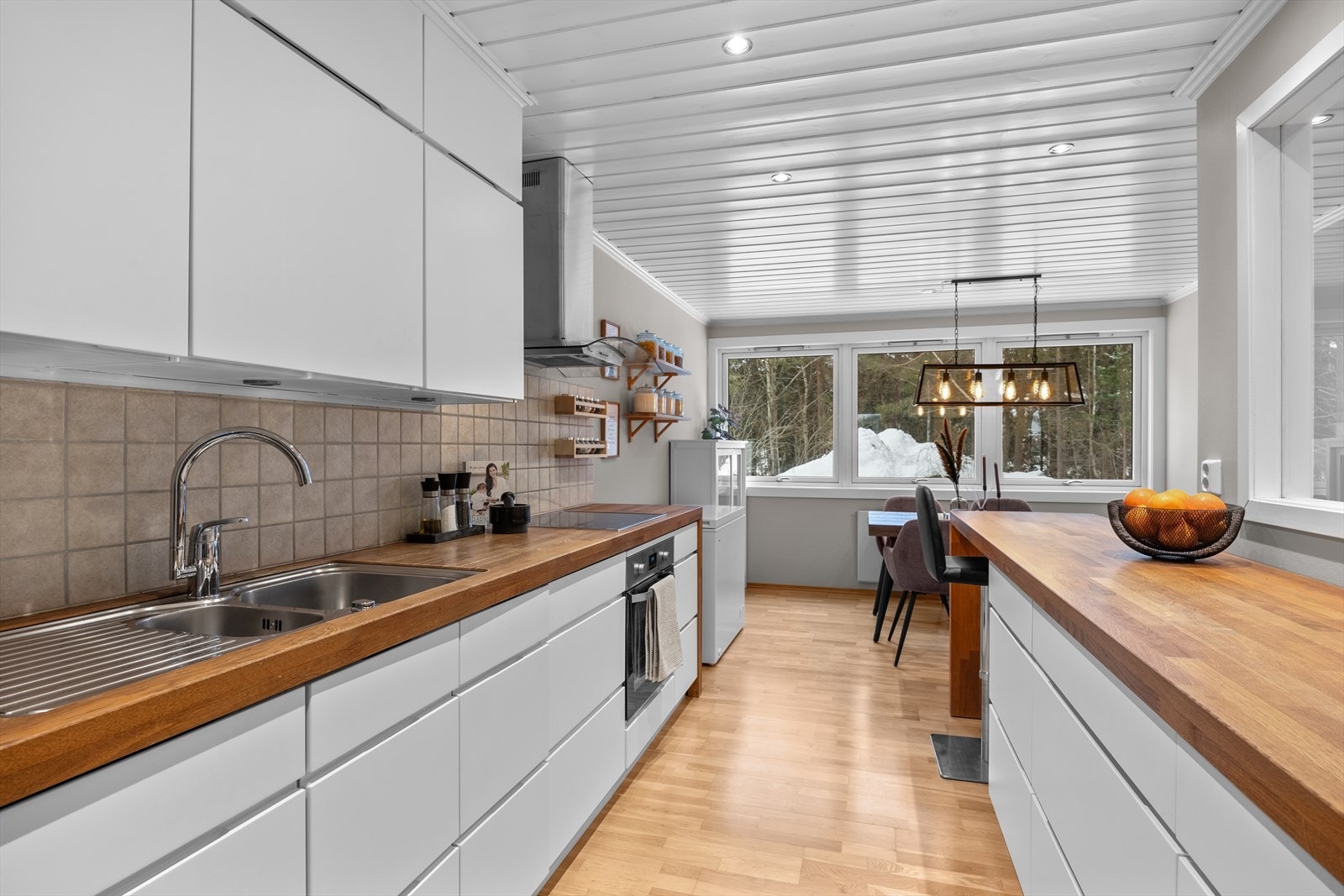 Separat kjøkken med en stilrene og lyse overflater fra 2004/2005. Hvit glatt kjøkkeninnredning med heltrebenkeplate og fliser mellom over- og underskap. Galleribilde