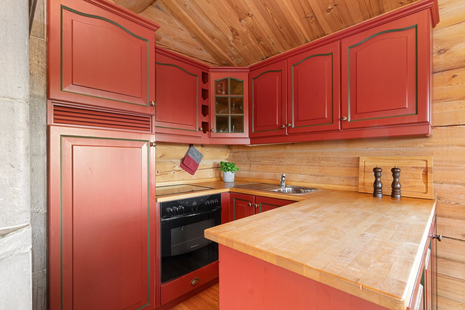 Kjøkkenet har en klassisk hytteinnredning med profilerte fronter i rød og grønn utførelse. Benkeplaten er av heltre. Det er kjøleskap (2021), oppvaskmaskin, platetopp og stekeovn. Galleribilde