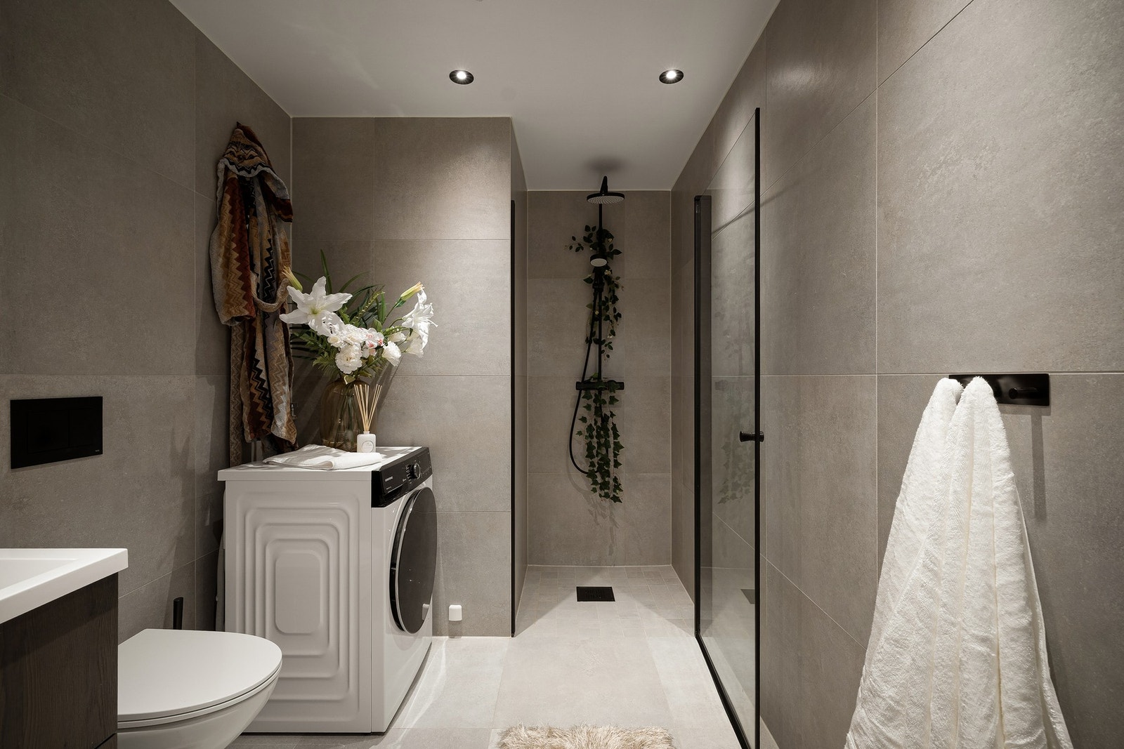 Badet er romslig og flislagt med store, moderne fliser og et gjennomført uttrykk med sort servantarmatur og regndusj. Galleribilde