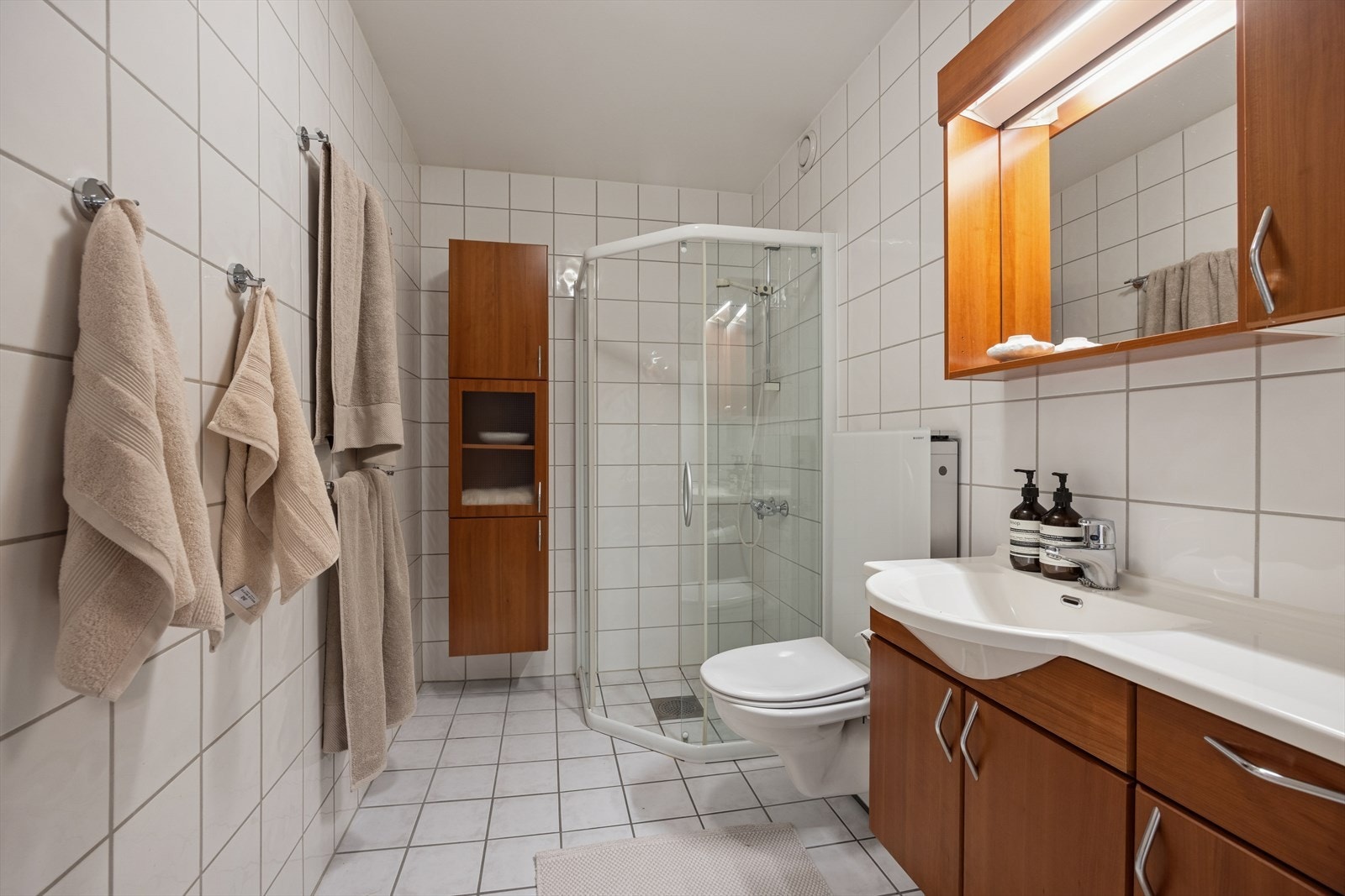 Baderom innredet med dusj med glass skyvedører, vegghengt toalett og servant. Galleribilde