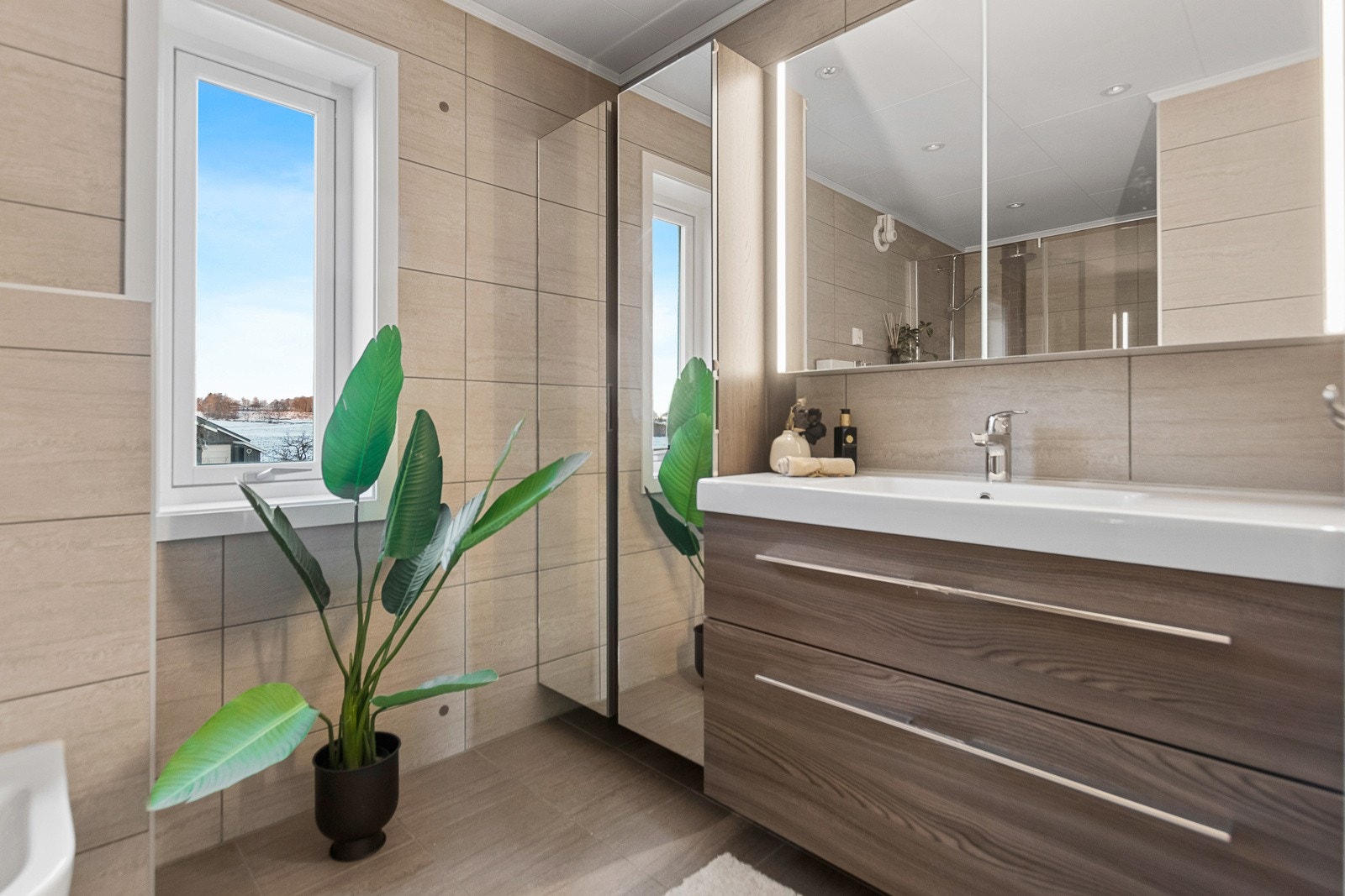 Flislagt bad med vegghengt toalett, dusjhjørne og innredning. Galleribilde