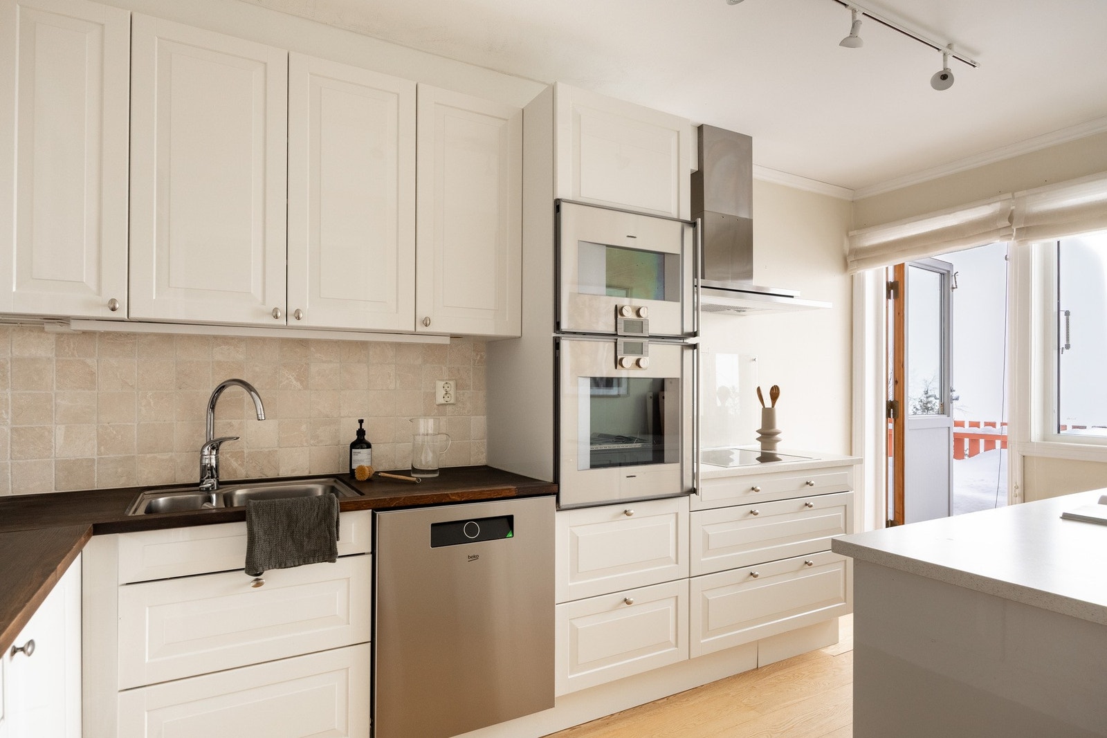 Det er profilerte fronter og benkeplater av kompositt og treverk med underlimt oppvaskkum i rustfritt stål, samt overskap med vitrinedører. Galleribilde