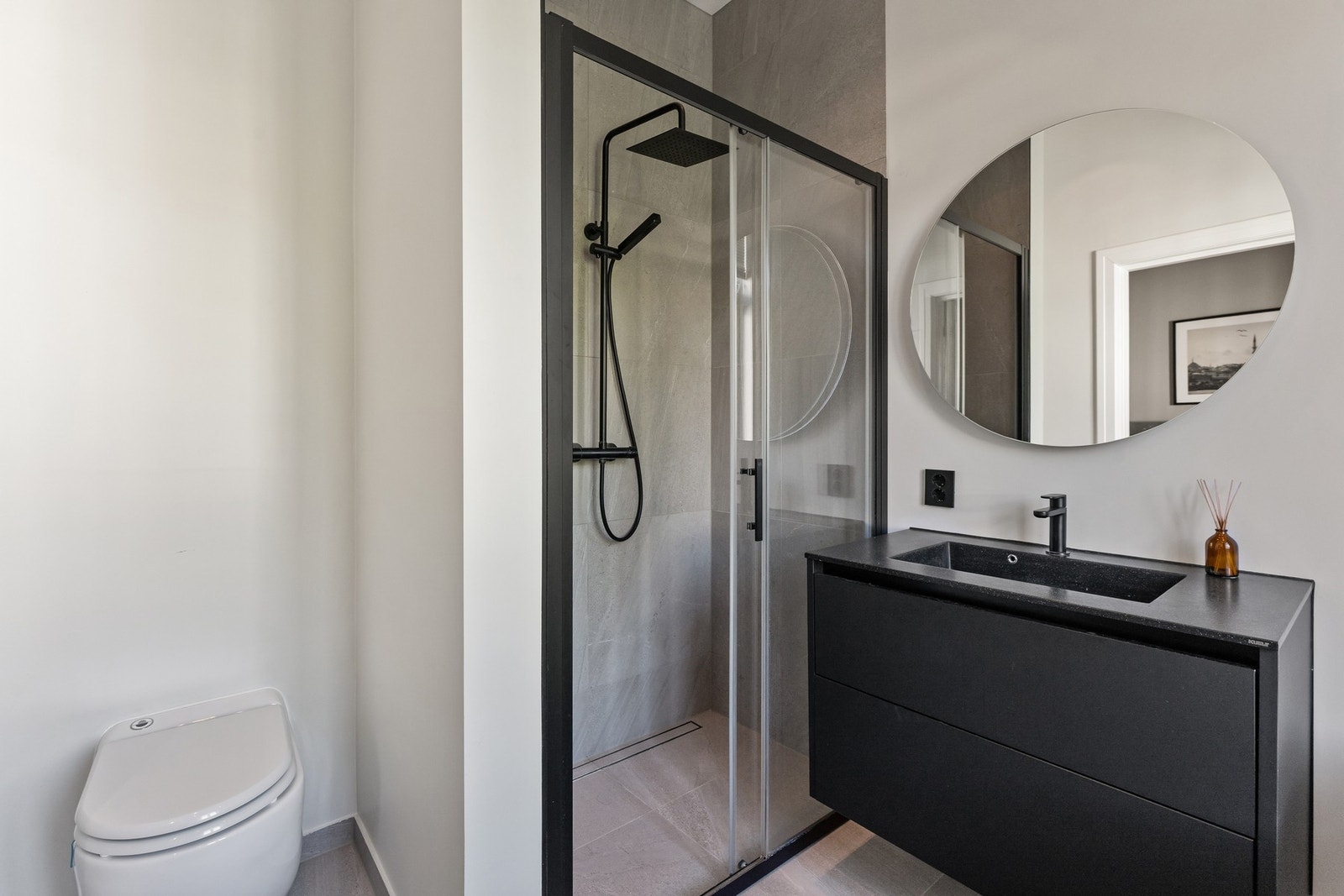 Badet inneholder dusjnisje, badekar, vegghengt toalett og servant med underskuffer. Galleribilde