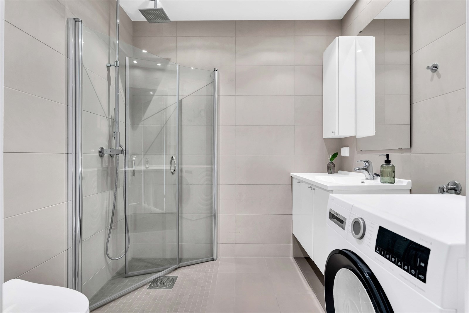 I tilknytning til soveromsavdelingen i første etasje ligger et av boligens to bad. Her er det flislagte gulv og vegger, elektrisk gulvvarme, regnfallsdusj, servantskap med nedfelt servant, vegghengt toalett og opplegg for vaskemaskin. Galleribilde