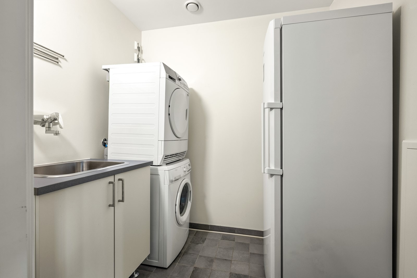 Vaskerom med smakfulle fliser på gulvet og gulvvarme. Det er opplegg/plass til vaskemaskin og tørketrommel samt stålvask nedfelt i innredning. Galleribilde