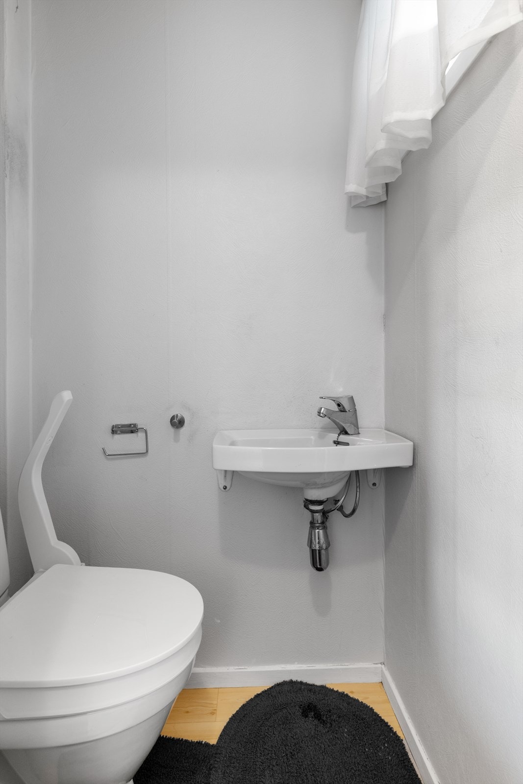 Separat toalettrom tilliggende boligens entré, utstyrt med gulvmontert toalett og en liten, vegghengt servant. Galleribilde