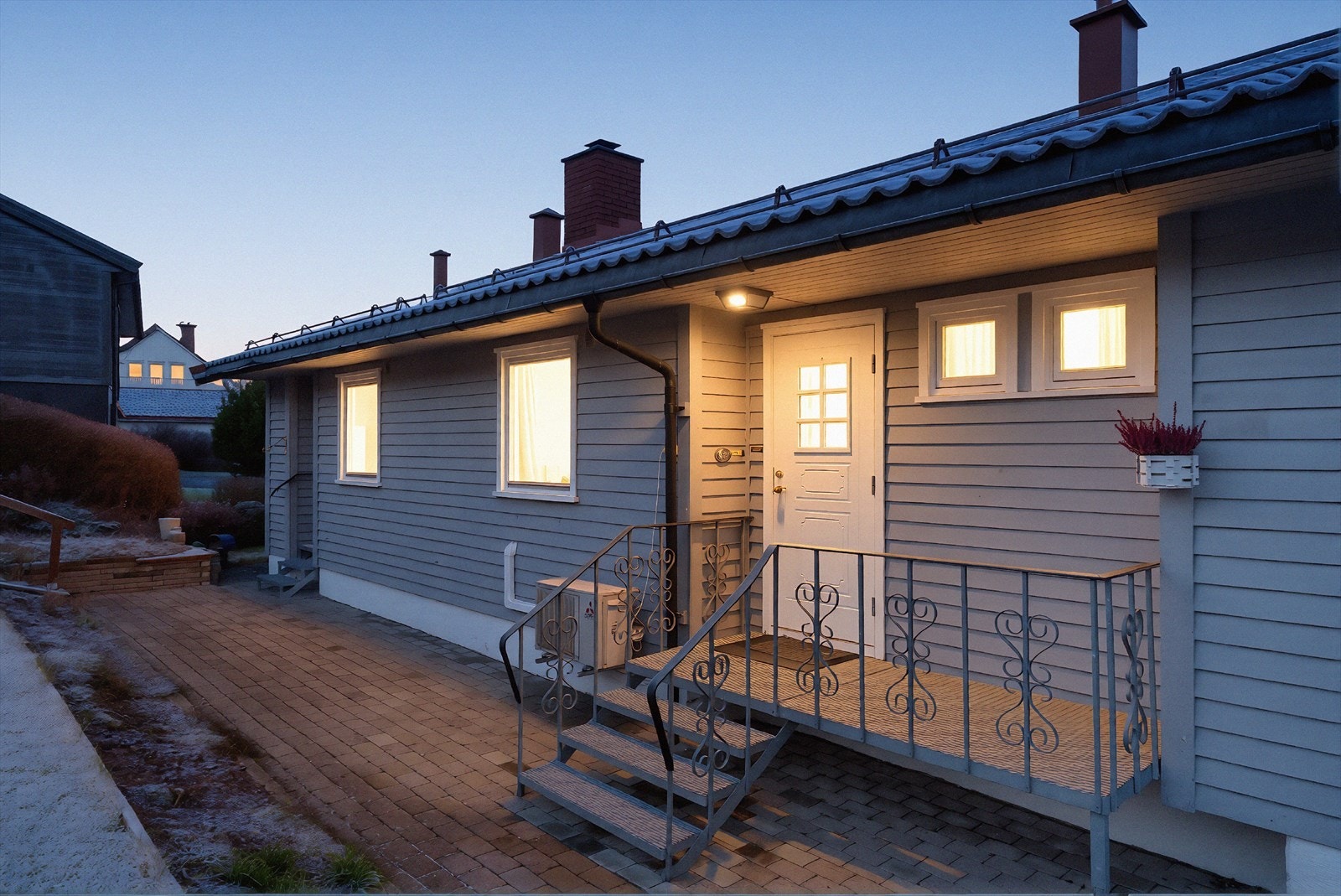 Gårdsplass og gangsti rundt boligen opparbeidet med belegningsstein. Bildet er redigert for å fremheve stemningen på kveldstid. Faktiske lysforhold kan variere. Galleribilde