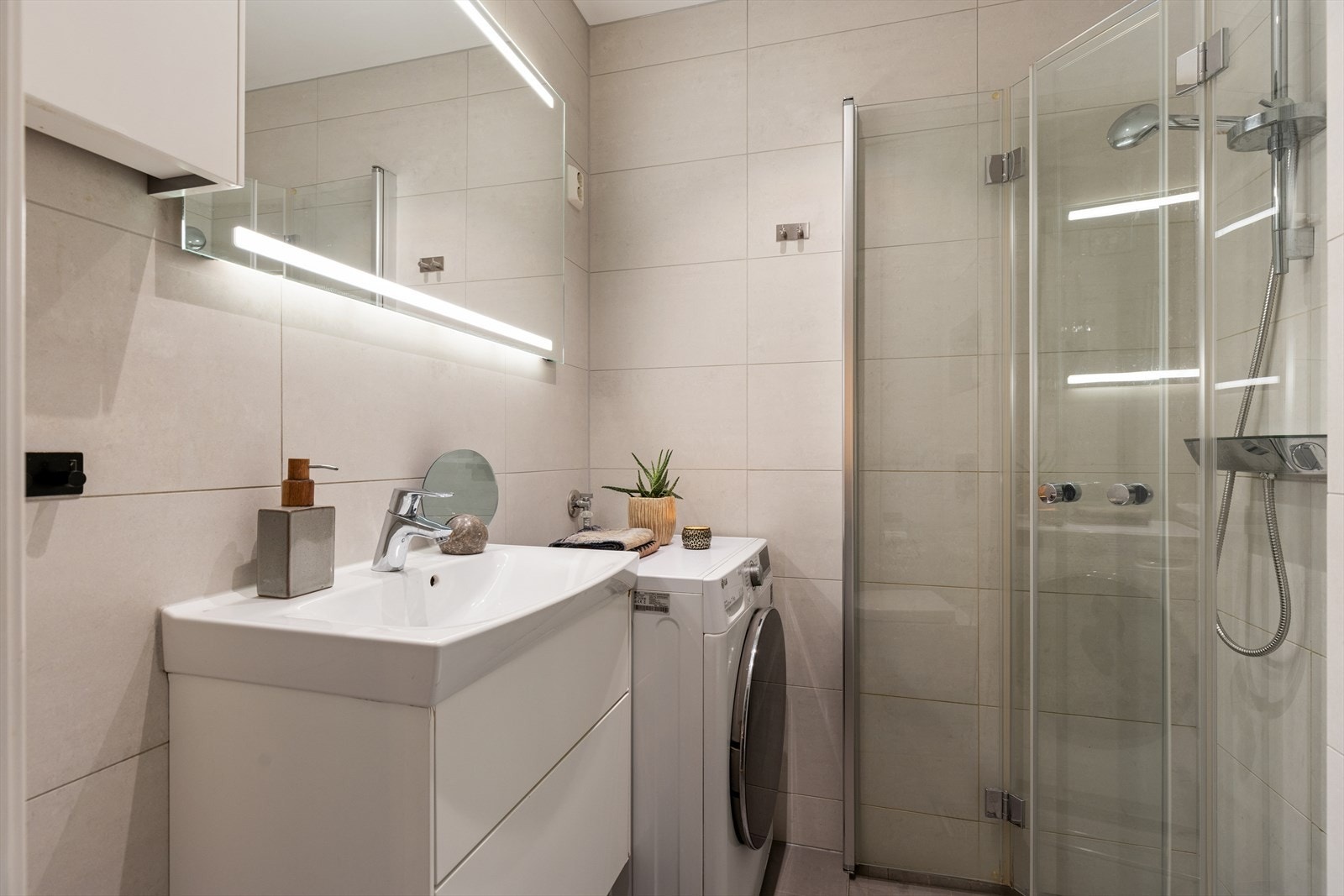 Badet ble renovert i 2018. Komforten sikres med elektriske varmekabler i gulvet, og belysningen kommer fra innfelte downlights i taket. Innredningen består av en servantseksjon, veggmontert toalett og et dusj. Opplegg for vaskemaskin. Galleribilde